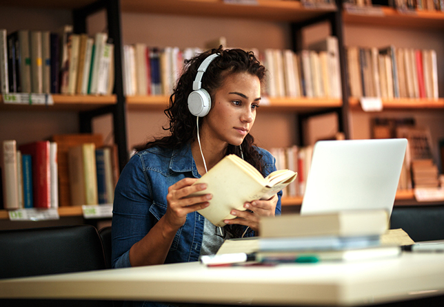 female student studying in a library, using laptop and learning online