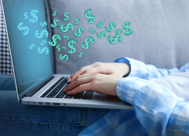 Woman using laptop with dollar bills coming out of the screen