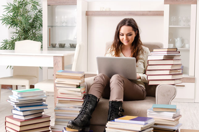 college student working on laptop surrounded by stacks of books