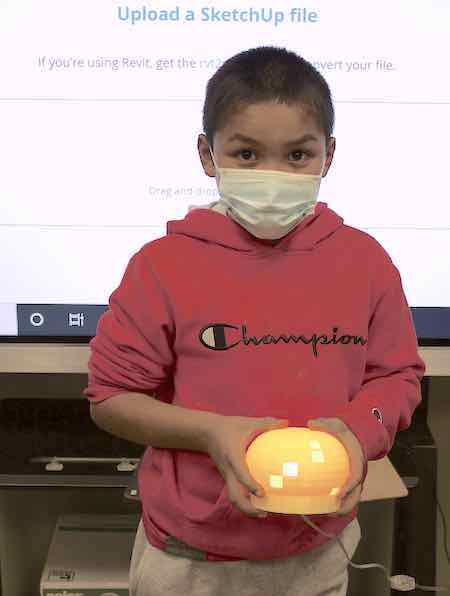 A young after school student modeled his own design of a light fixture using SketchUp, a digital sketch application, then 3D printed his creation, put in the electrical wiring, and proudly shows it here.