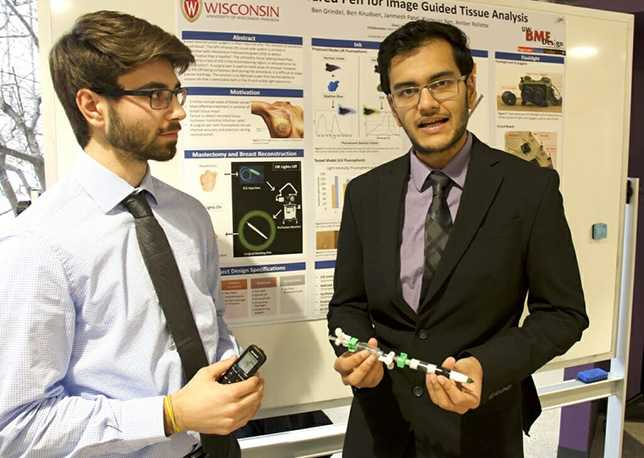Biomedical engineering students Ben Knudsen (left) and Janmesh Patel demonstrate a pen they're developing to mark tissue during breast surgery performed under infrared light, which helps a surgeon see cancer cells. The pen will also contain conventional ink to mark tissue for evaluation and treatment in daylight. The device combines off-the-shelf parts with 3D-printed parts and is being built under the guidance of plastic surgeons at UW Health. Photo by David Tenenbaum.