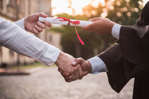 closeup of graduate in academic dress taking his diploma and shaking hand