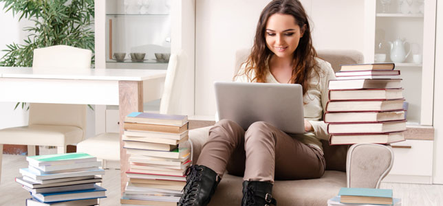 college student working on laptop surrounded by stacks of books