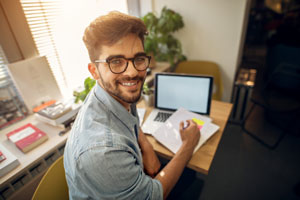 Portrait of happy motivated smiling hipster student learning for a test or an exam at high school library desk while sitting turn backwards and looking at the camera.