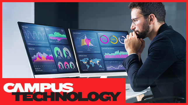 Man sitting at desk looking at data visualizations on two monitors