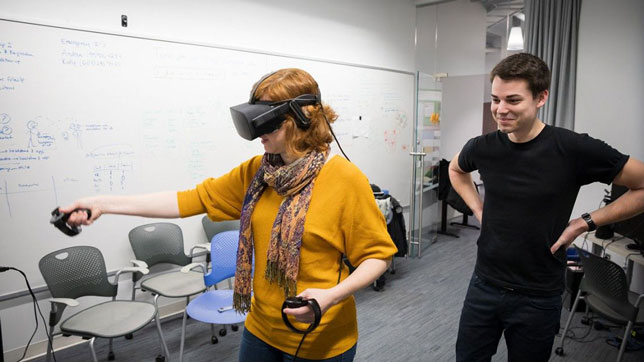 Jack Madden, a Cornell doctoral candidate in the field of astronomy, watches as Andrea Stevenson Won, assistant professor of communication and director of the university